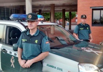 El guardia civil Sergio Otero, al fondo a la derecha, con su compañero y su coche patrulla.